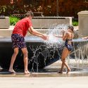 A boy splashes a girl with water from the fountain.