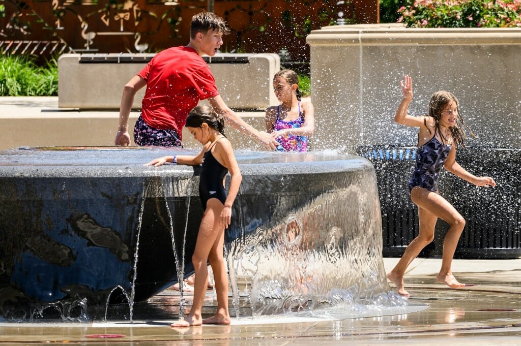 Children run around a water fountain.