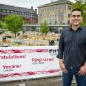 Photo of Brian MacInnes standing next to a red and white banner on the Memorial Union Terrace with the word 