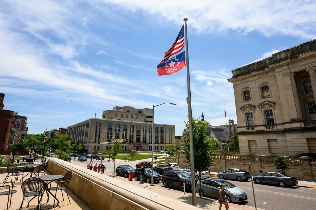 The flag is viewed with campus buildings in the background.