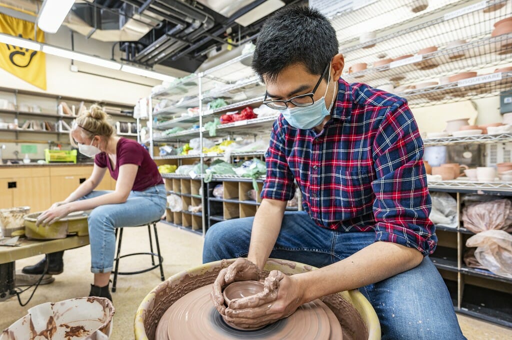 UW graduate student Andrew Sung forms clay at a pottery wheel.