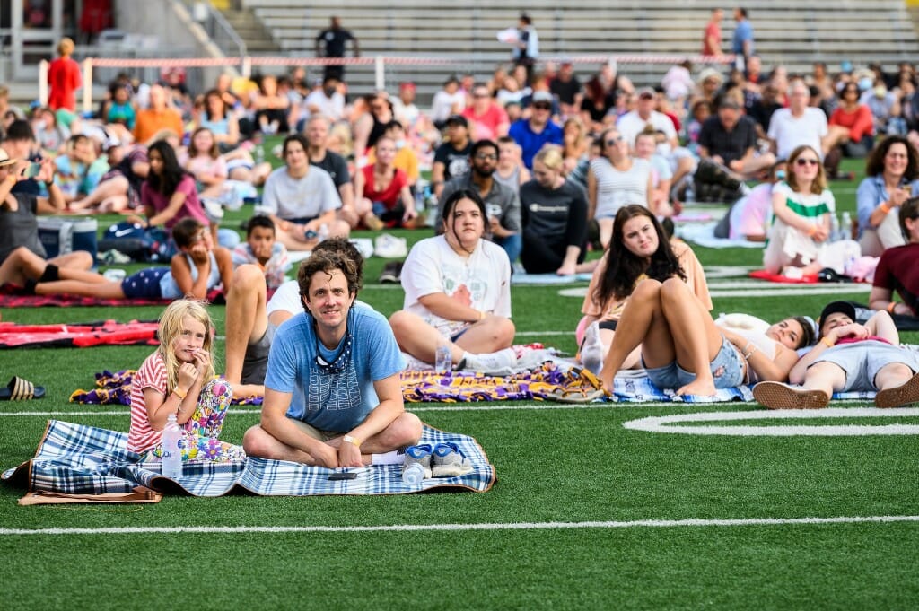 At left of center, Dustin Brown, a lecturer with Legal Research and Writing in the Law School, and his daughter Leila Bhavnani, 7, join more than 800 university employees and their families spread out on the field to watch the 2020 film 