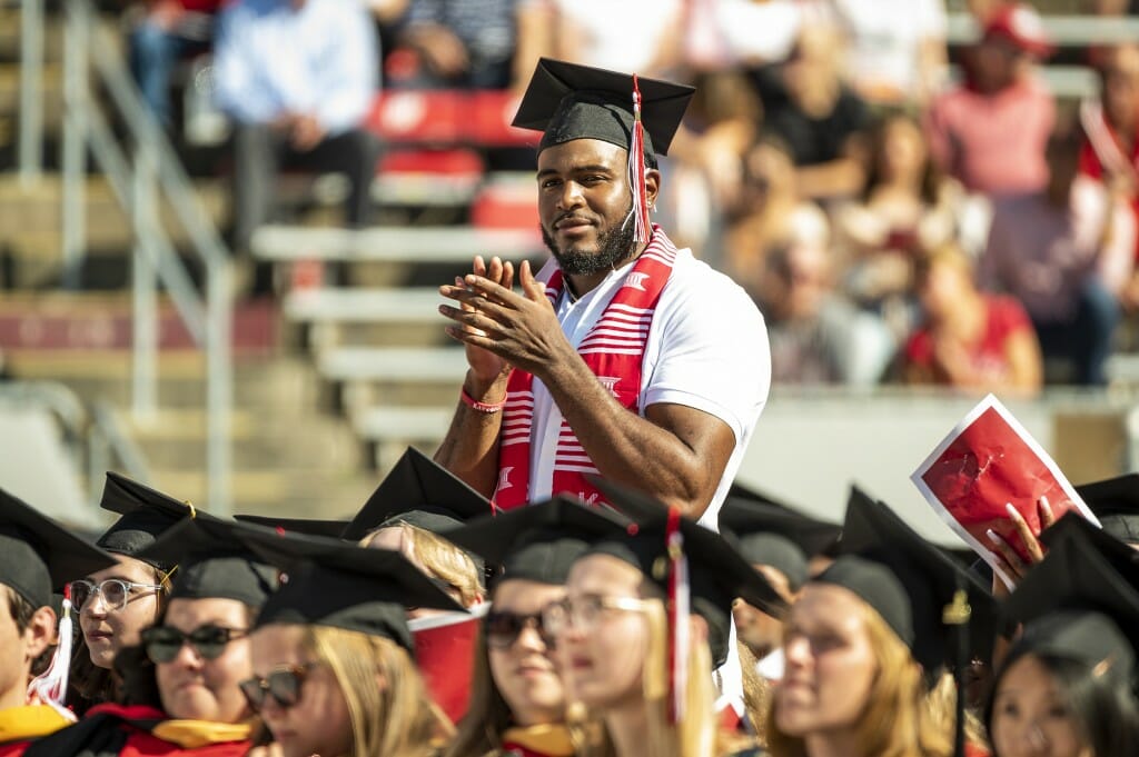 Person standing in the midst of seated graduates