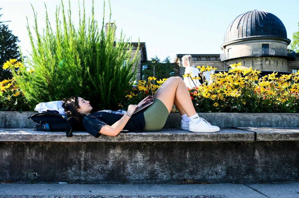 Katina Mistrioty, a recent transfer student from UW-LaCrosse, relaxes in the shade and works on her laptop computer while sitting on a bench along Observatory Hill Drive.