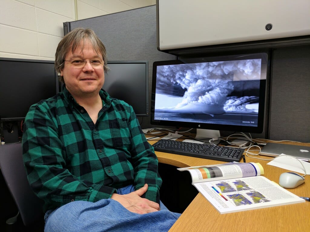 Orf sitting next to computer monitor on desk