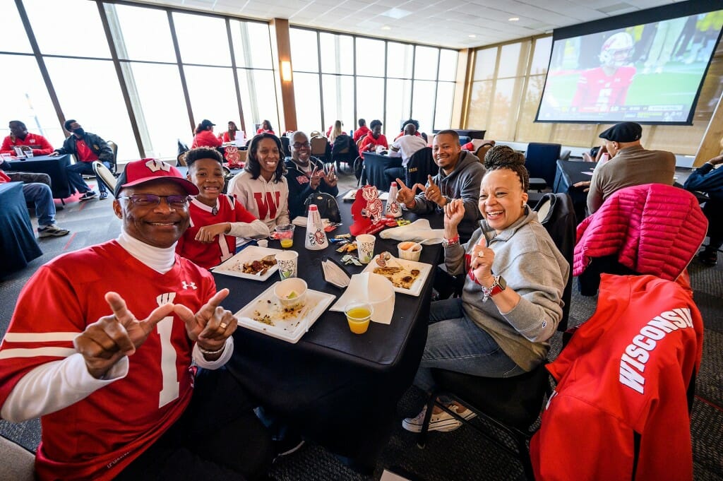 At right wearing grey, Candace McDowell, director emerita of the Multicultural Student Center, and her extended family celebrate a Wisconsin touchdown during a football game against Iowa as seen at the Multicultural Homecoming Game Watch and Tailgate at the Pyle Center.