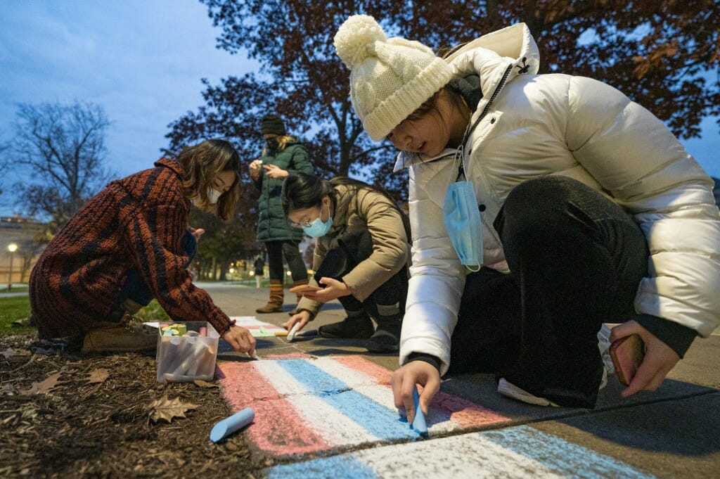 Visiting scholar Yuyang Jiang (center) draw international flags in chalk along the Bascom Hill sidewalk in front of the Education Building.