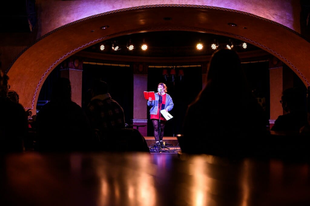 Social Justice Hub operations intern Sophia Boté introduces the next performer. 
“This open mic night is intended to give an underrepresented group the chance to find community through art and shared experiences,” says Boté, who was event coordinator.