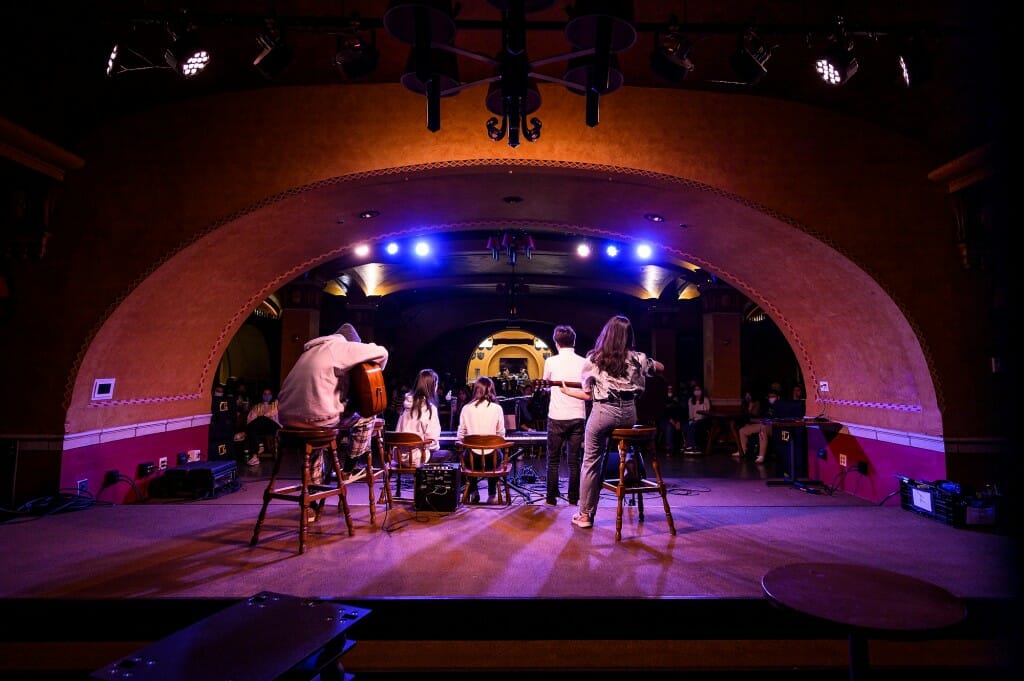 A group of student musicians, from behind left to right, guitarist Tianrui Liu (Mark), vocalist Zhengxi Guo (Ellen), Weiyu Xu (Vidia) on keyboard and vocals, vocalist Hongwei Tian (Johnney), and guitarist Ziqian Xu (Selina)  perform a song.