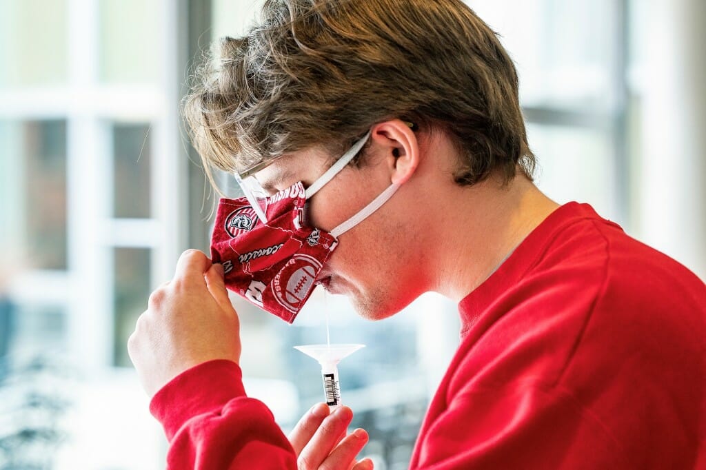 A person raising his face mask to drool into a vial