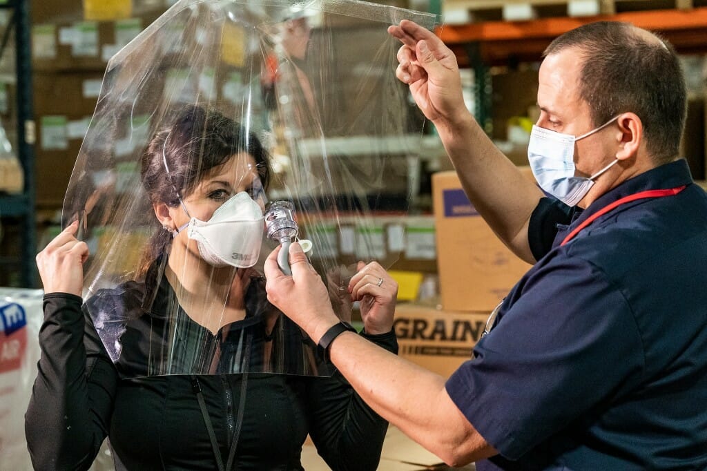 A person spraying mist toward a clear shield in front of a person wearing a face mask