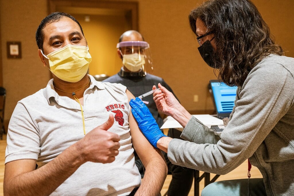 A person giving a thumbs-up as vaccine is administered in his arm