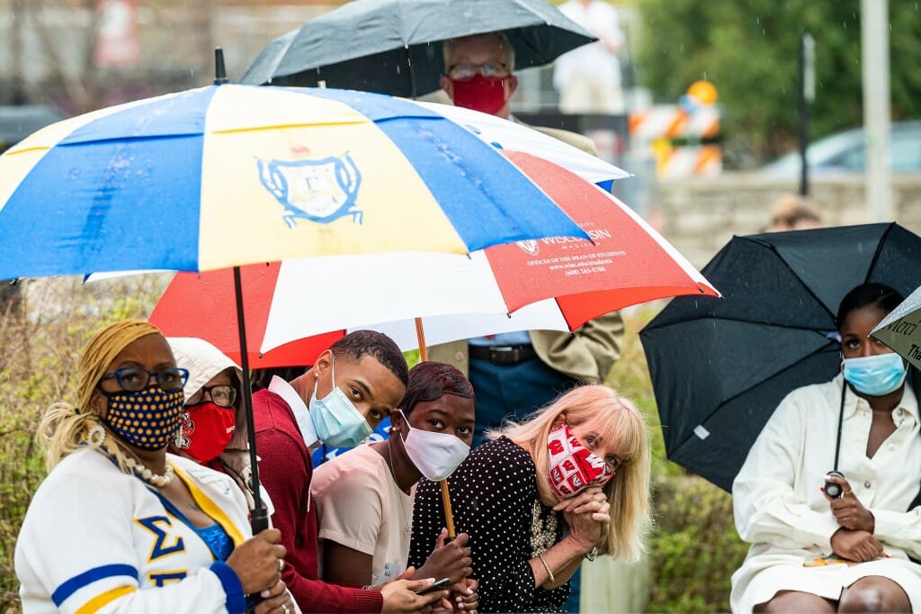 Several people sitting under an umbrella at an outdoor ceremony