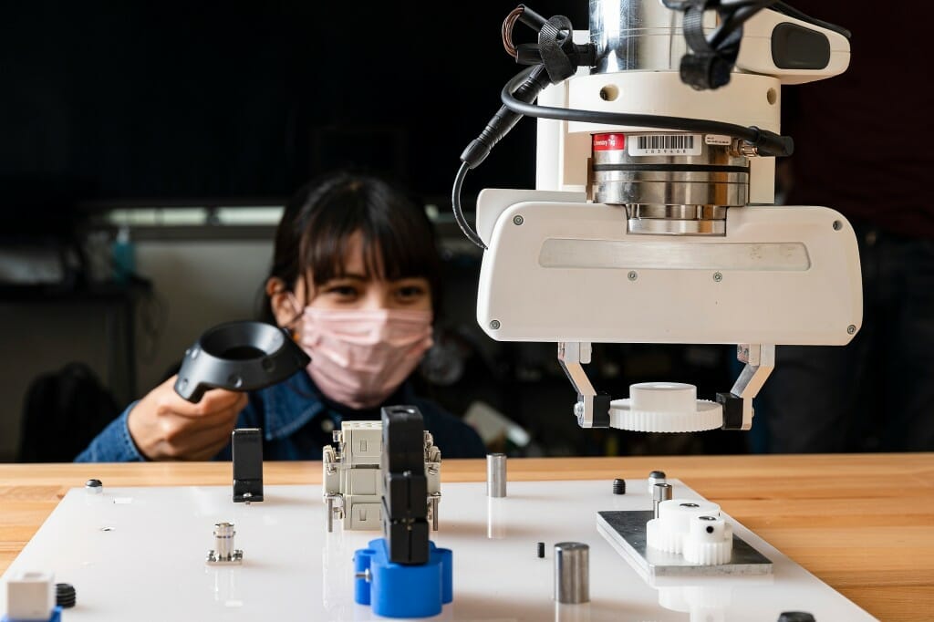 A student peeking over a table that a robot arm is placing gears on