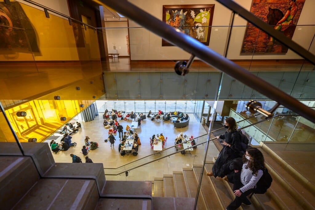 Students walk down the stairs from the gallery to the lobby.