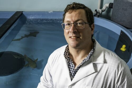 Portrait of Aaron wearing white lab coat in front of tank