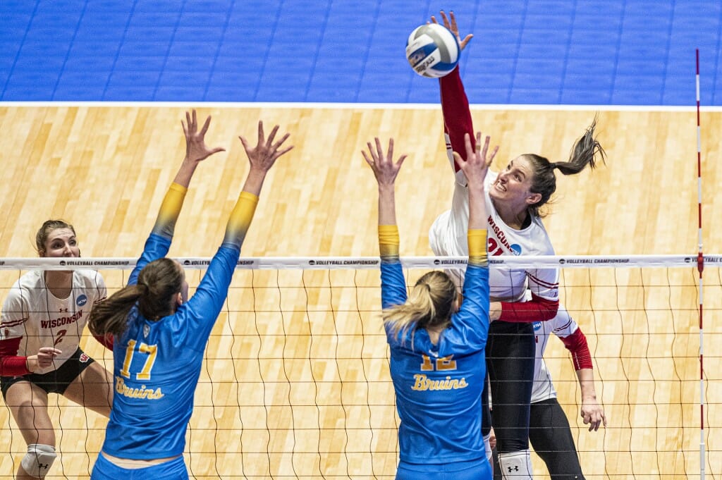 Loberg spikes the ball over the outstretched arms of 2 UCLA players