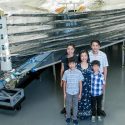 People standing in front of a large piece of space telescope equipment