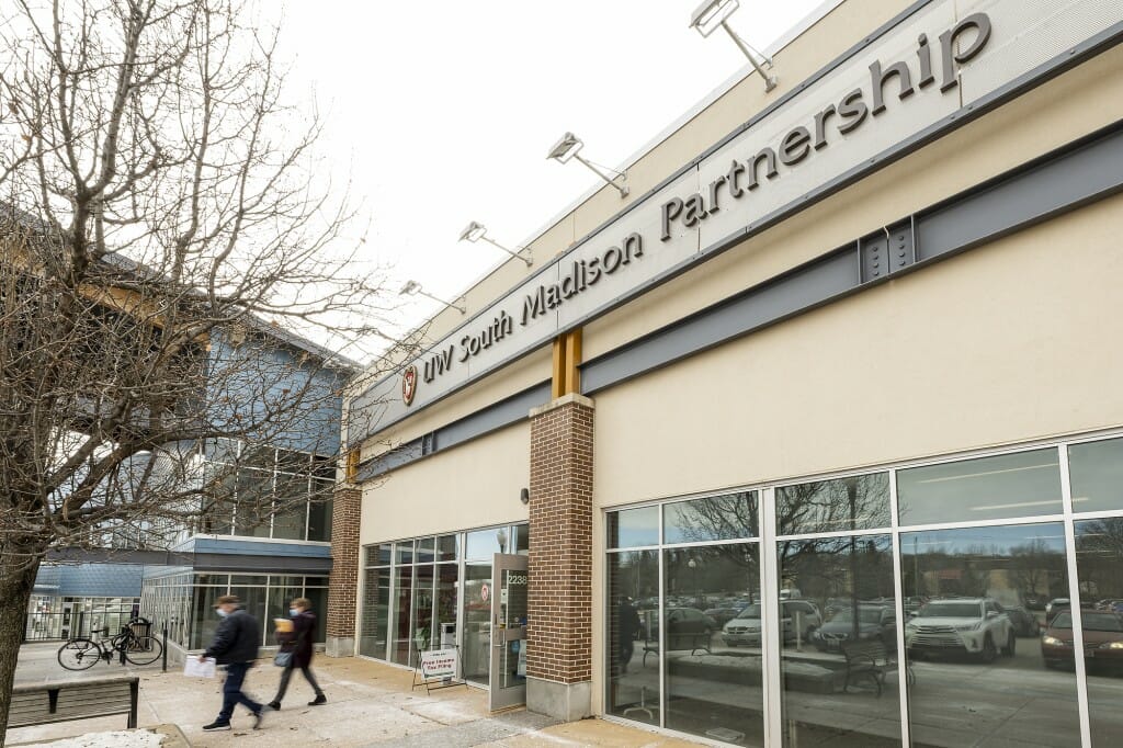 Two people walking out the front entrance to a modern building with a sign saying "UW South Madison Partnership"