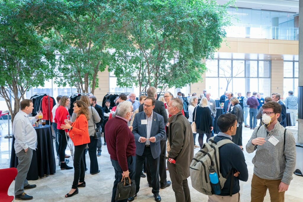 A group of several dozen people standing and talking among themselves in the brightly lit Discovery Building lobby