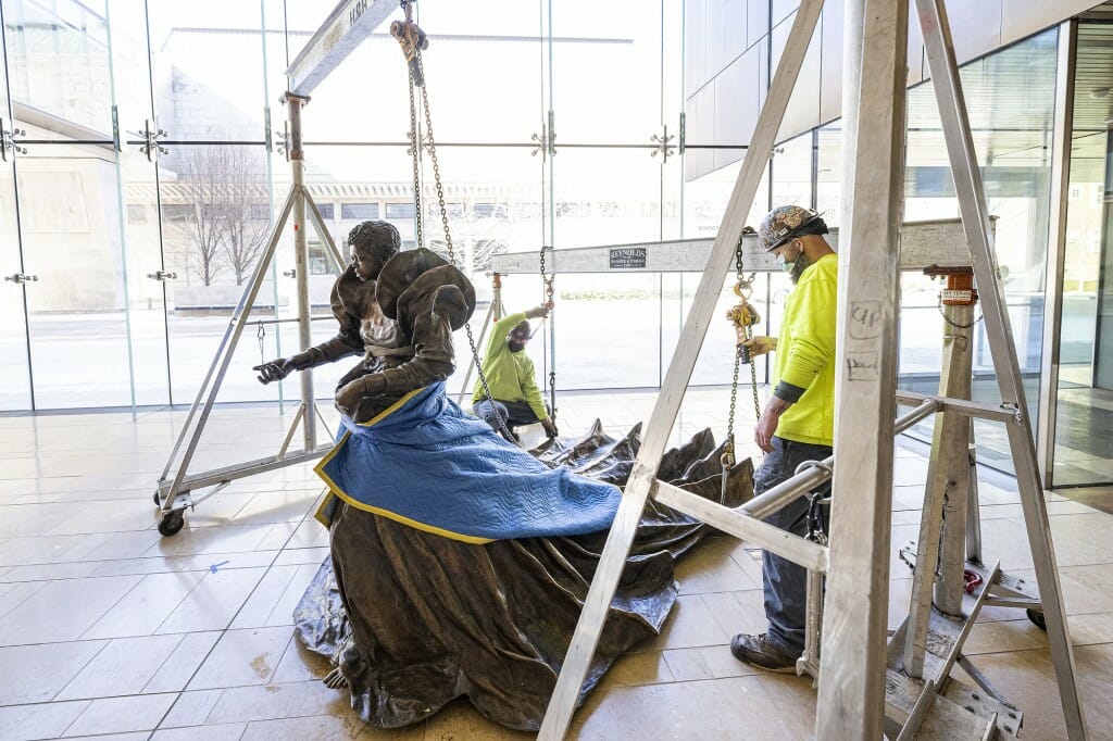 Workers using steel beams and pulleys to hoist the statue