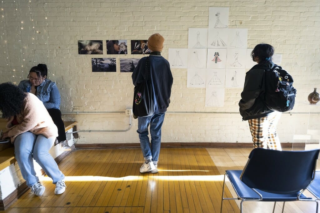 Guests look at student artwork on display, including photography by Koda Parker, at left, and wedding-dress sketches by Pahoua Yang.