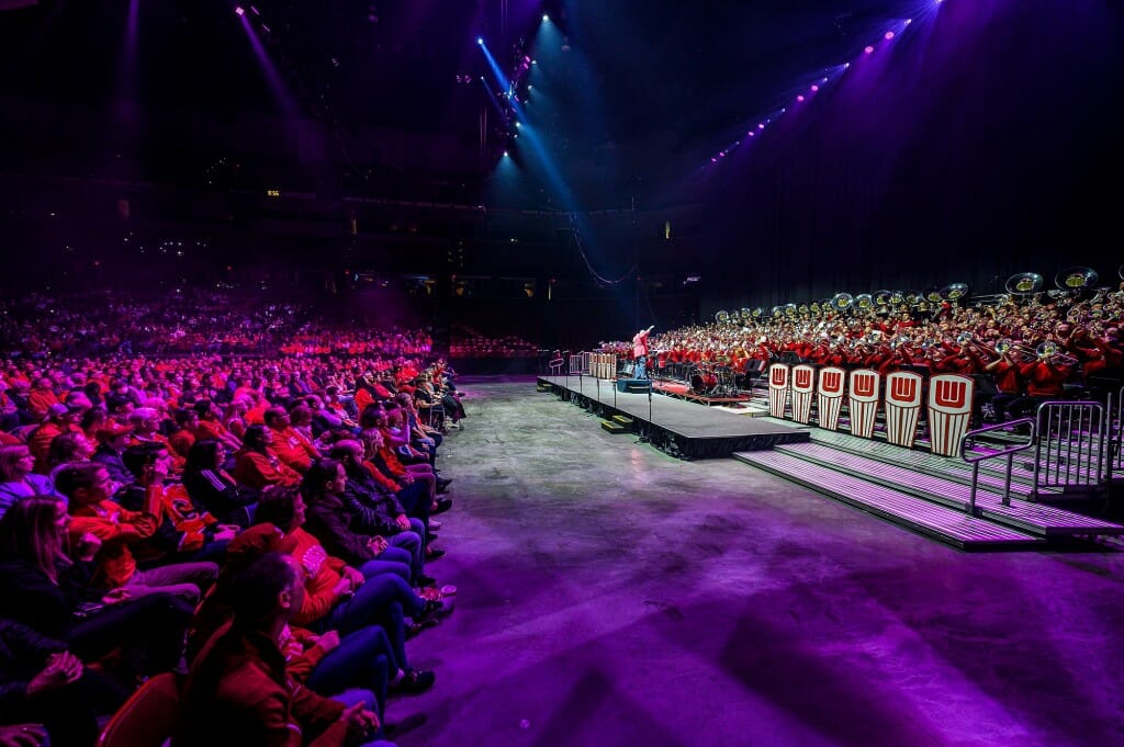 Red concert lighting illuminates the crowd as band director Corey Pompey conducts.