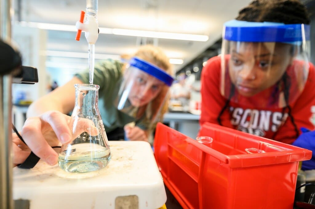 Two students wearing clear plastic face coverings while conducting an experiment