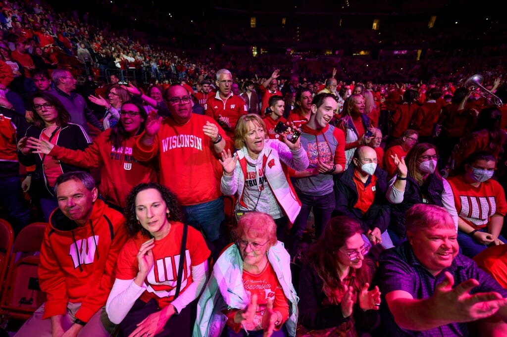 A crowd wearing red stand and cheer the unseen band.