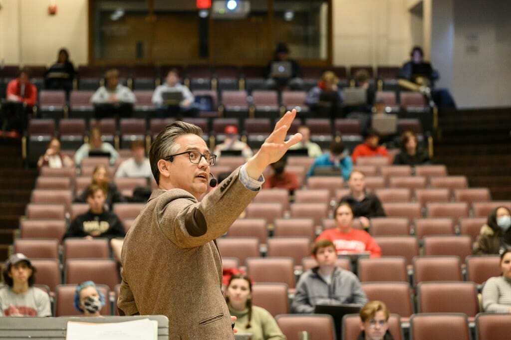 Joshua Calhoun facing students sitting in a lecture hall, turning to gesture toward the front