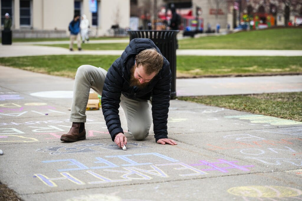 Jake McCulloch, a sustainability program manager at the Office of Sustainability, uses chalk to draw Bucky Badger on the sidewalk.