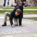 Jake McCulloch, a sustainability program manager at the Office of Sustainability, uses chalk to draw Bucky Badger on the sidewalk.