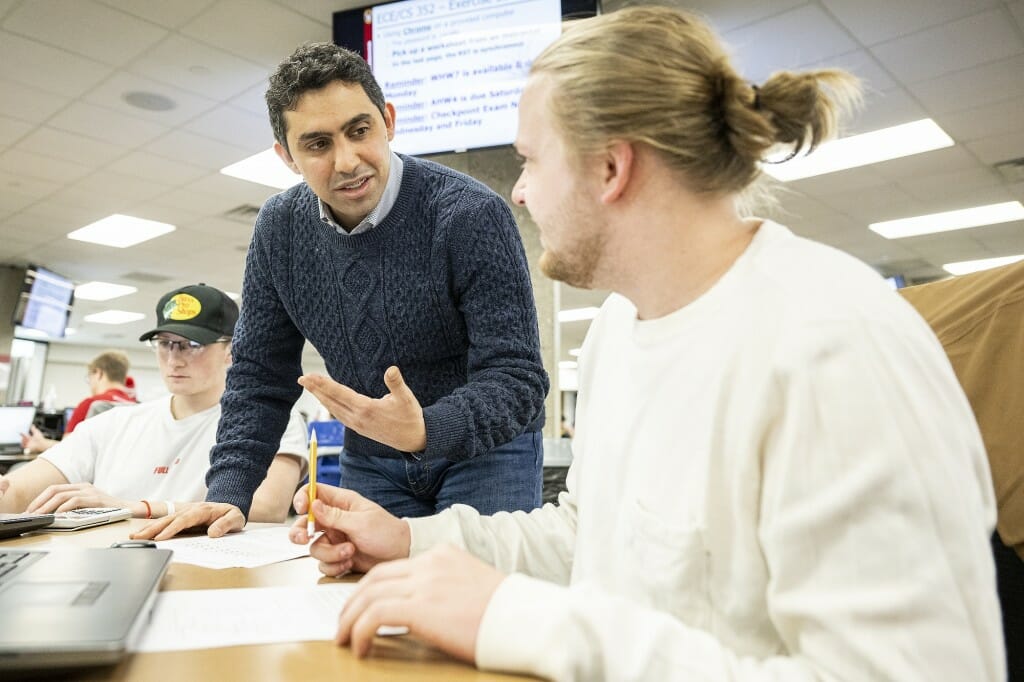 Kassem Fawaz in a classroom leaning on a table and gesturing to a student