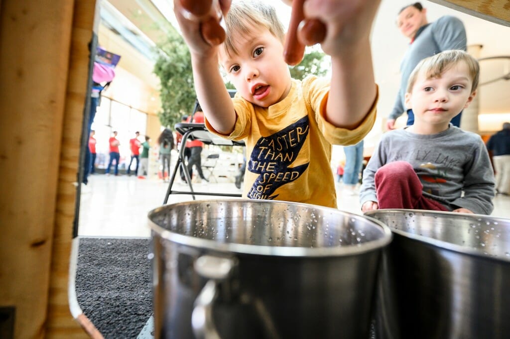 At left, 3-year-old Belmont West tries “milking” a wooden cow while his twin brother Apollo West looks on in the discovery building.