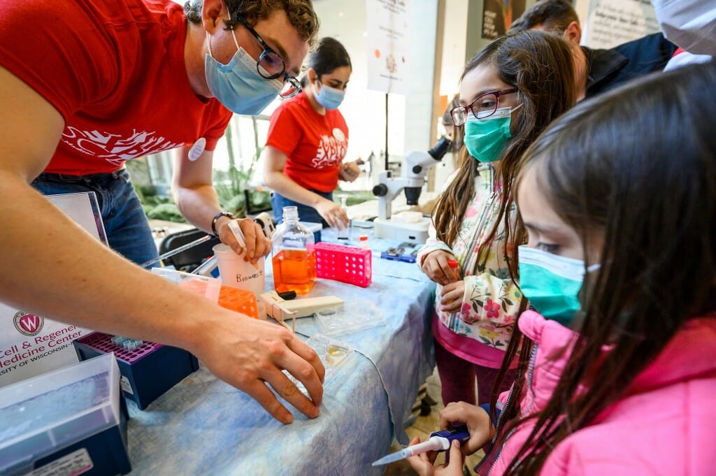 At left, undergraduate student and Goldwater Scholar Samuel Neumann helps 8-year-old Maria Escalona (center) and 6-year-old Ignacio Escalona (right) feed and pipet mock cell samples in the Discovery Building.