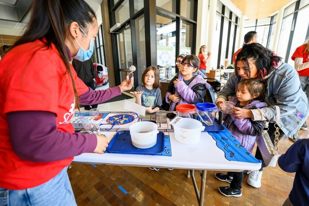 At left, undergraduate student Megan Nayar from the Wisconsin Sea Grant helps 6-year-old Adriana Rivera, 8-year-old Gabriela Rivera, and 4-year-old Sofia Rivera strain sediment from a water sample in a hands-on display in the Wisconsin Energy Institute.