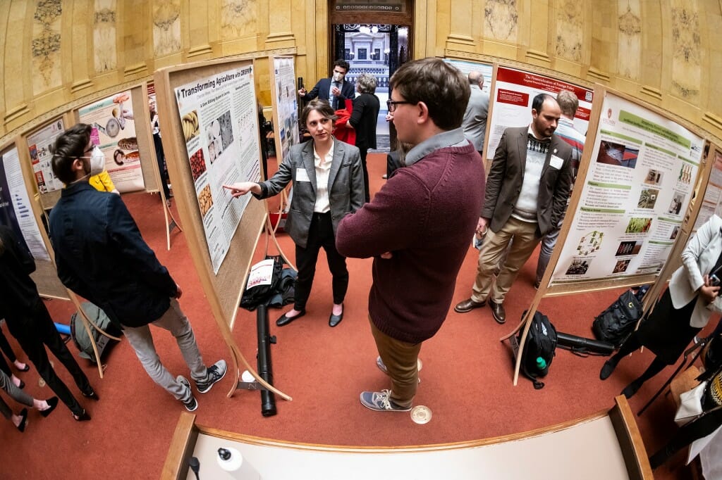 A person gesturing toward a poster, explaining it to a listener