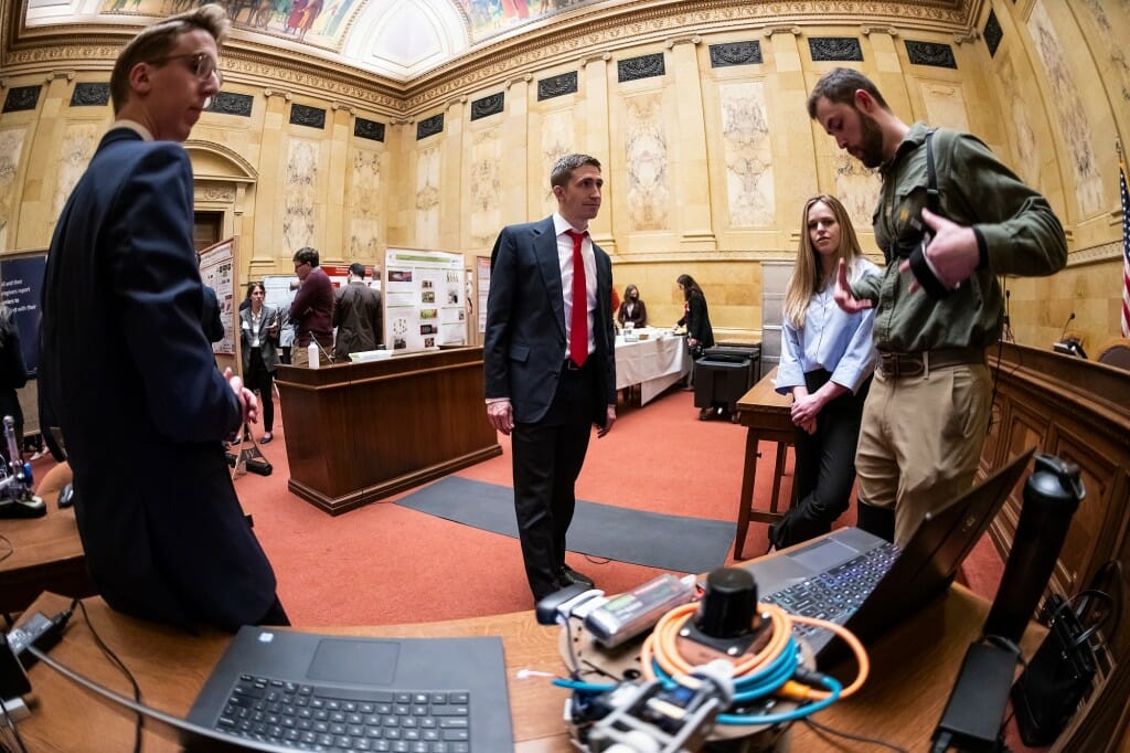 Several people standing in a semicircle in a marble-walled hearing room