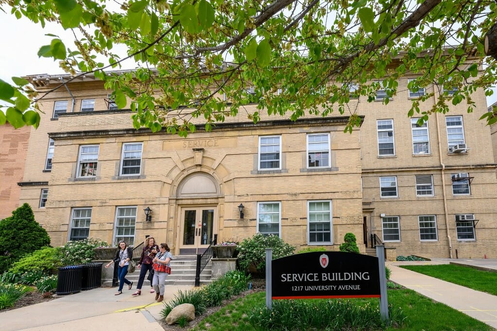 The exterior of a brown building, with people walking out.