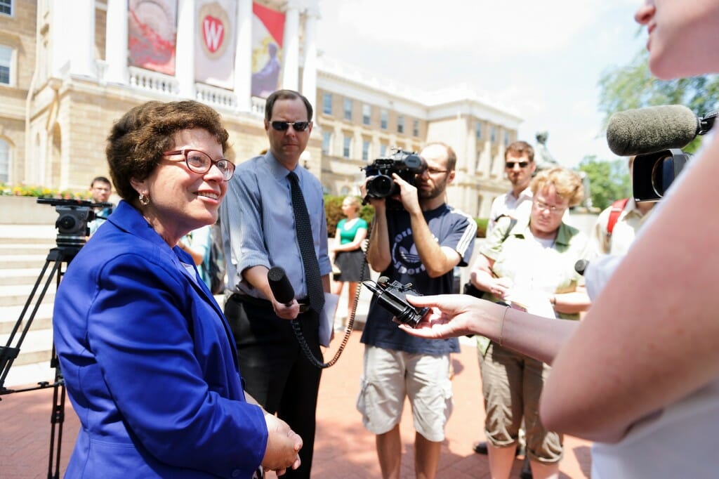 Blank smiling with a reporter holding a microphone and a videographer holding a camera in front of Bascom Hall