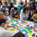 People paint a mural on a table.