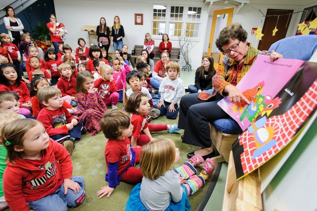 Blank sitting in a chair and holding a book up so a roomful of preschoolers can see the pictures