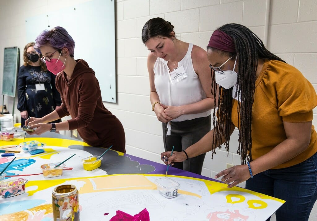 Three people lean over a mural to inspect it.