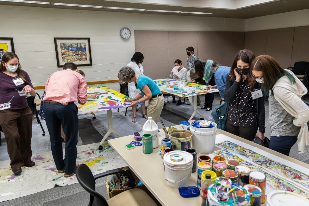 Groups of people stand next to the mural with paint brushes.