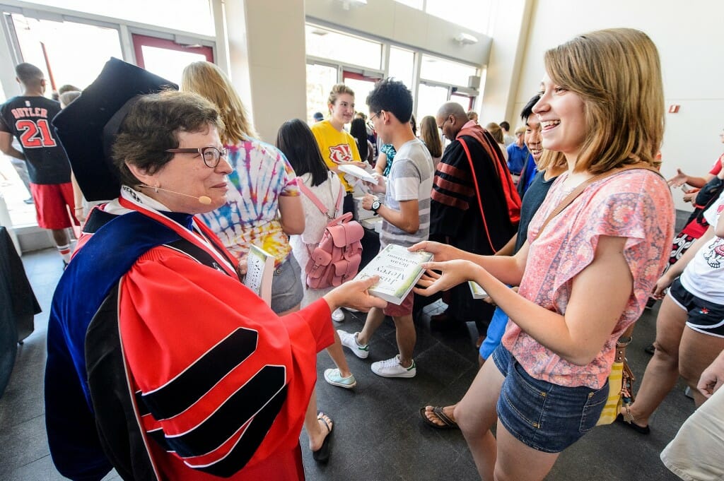 Blank, in academic gown, handing a book to a student