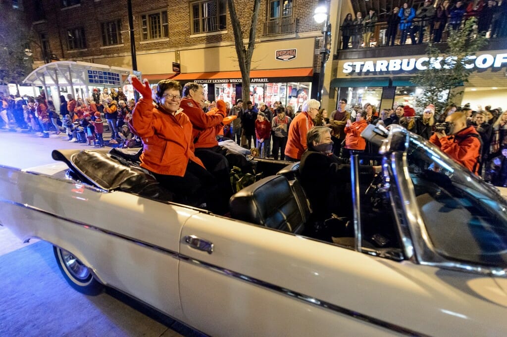 Blank and Hanns riding in an open white vintage convertible driving past a Starbucks sign