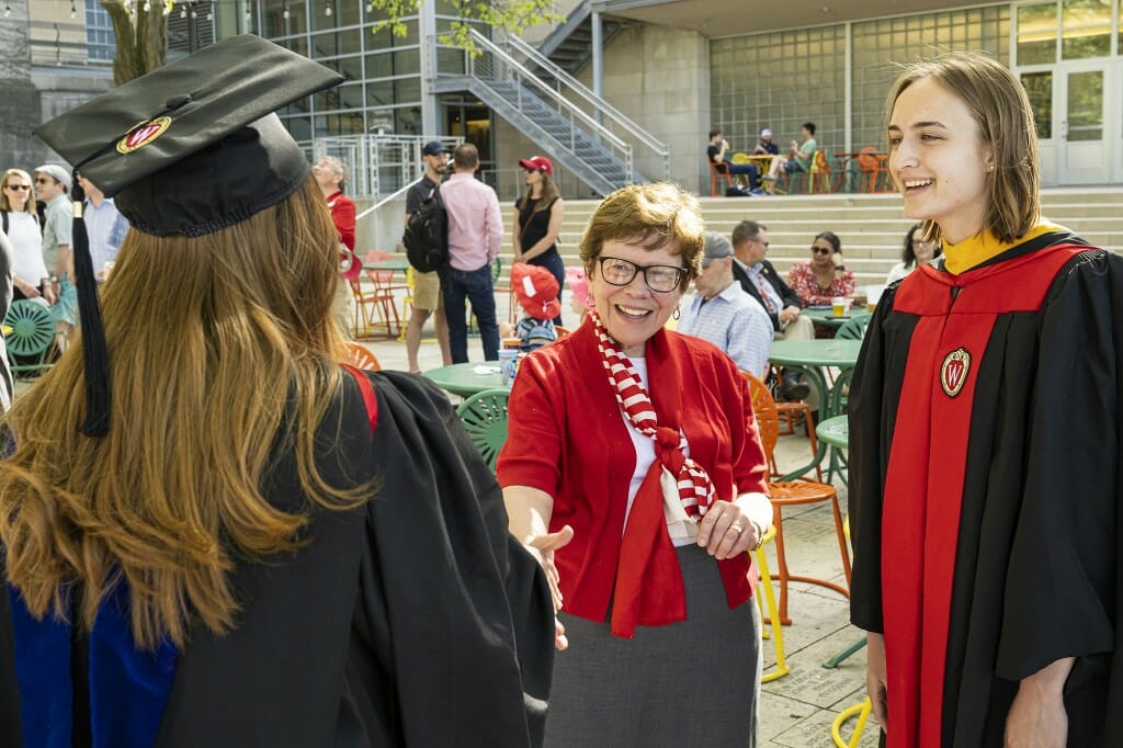 Blank talking with 2 people in caps and gowns