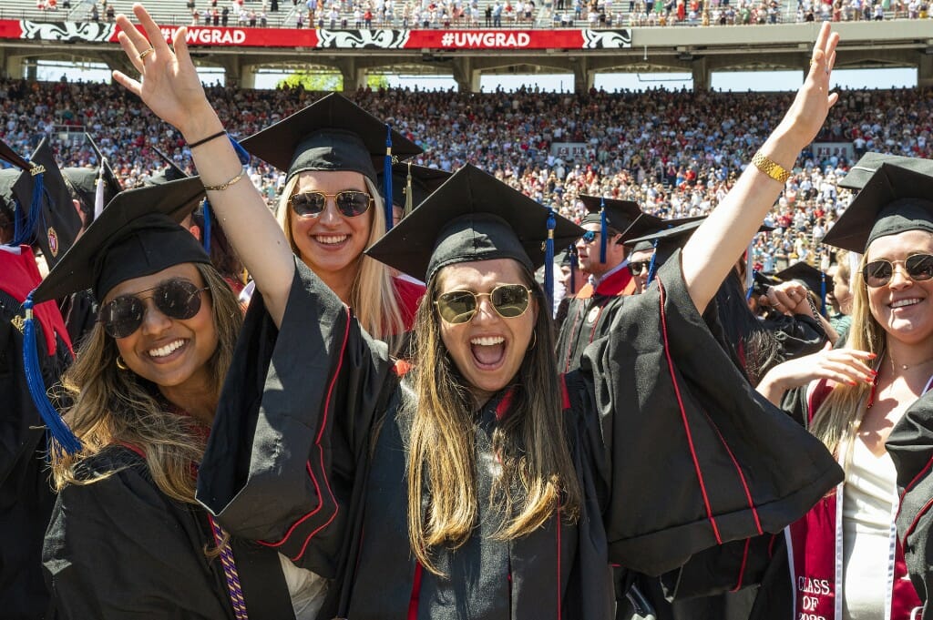 Several graduates smiling and holding arms up