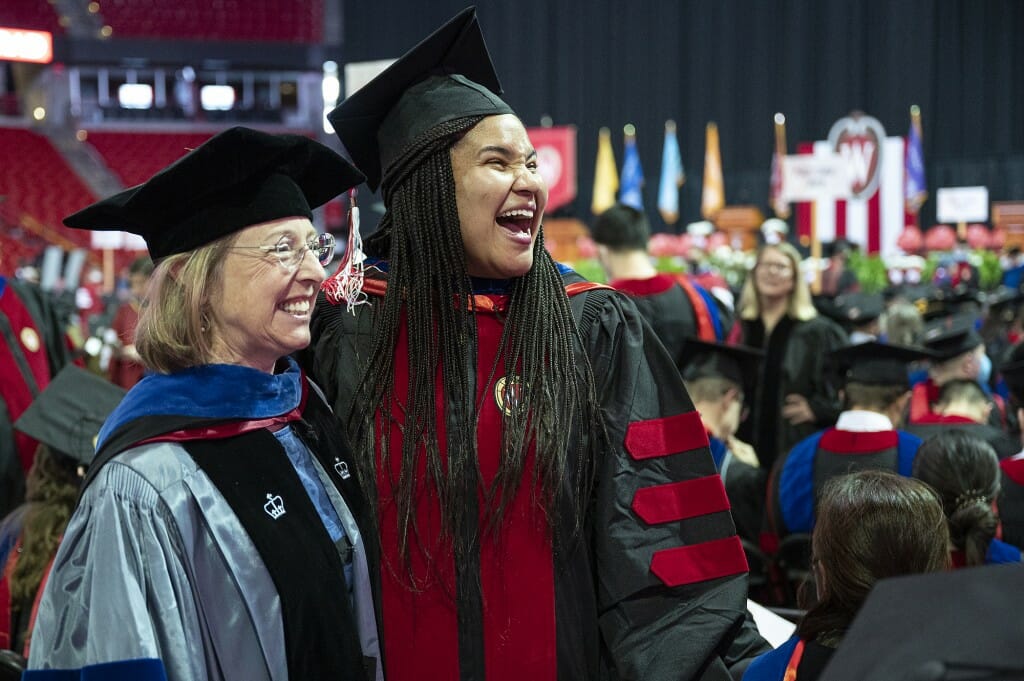 Two people standing together wearing different versions of academic regalia