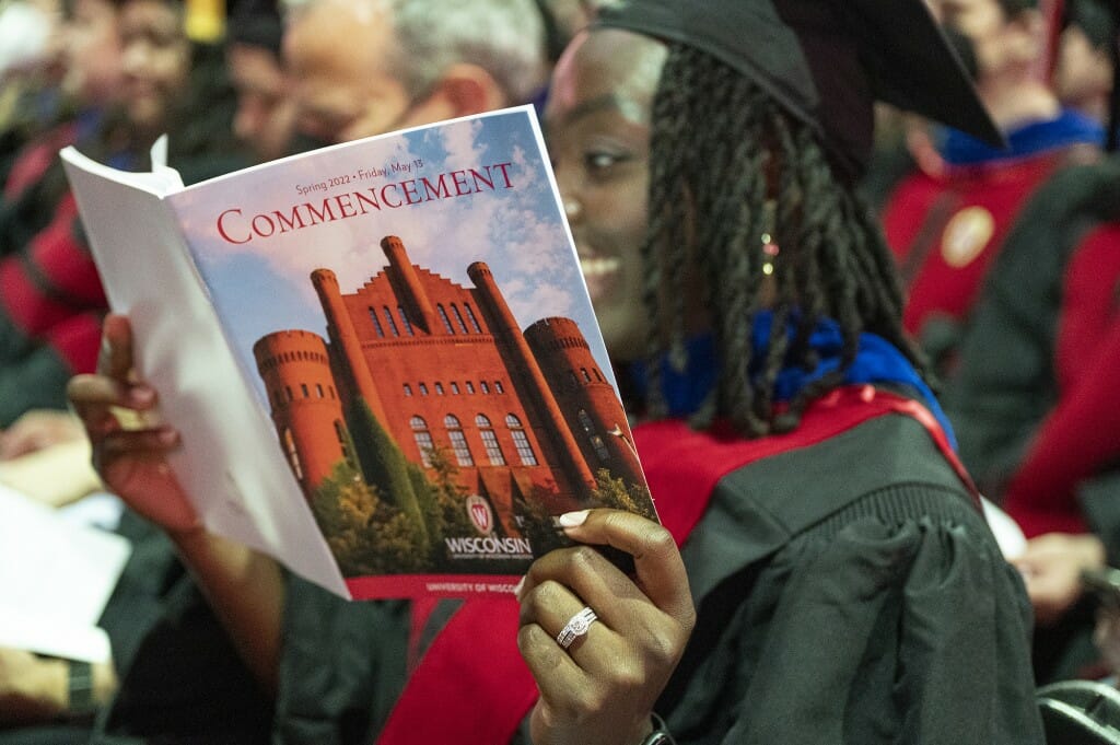 Person in cap and gown looking at booklet with the Red Gym pictured on the cover